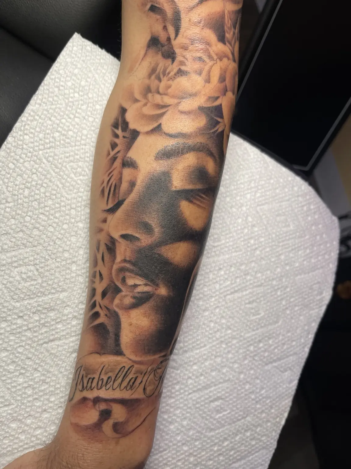 Black-and-gray portrait and floral forearm tattoo by Keith