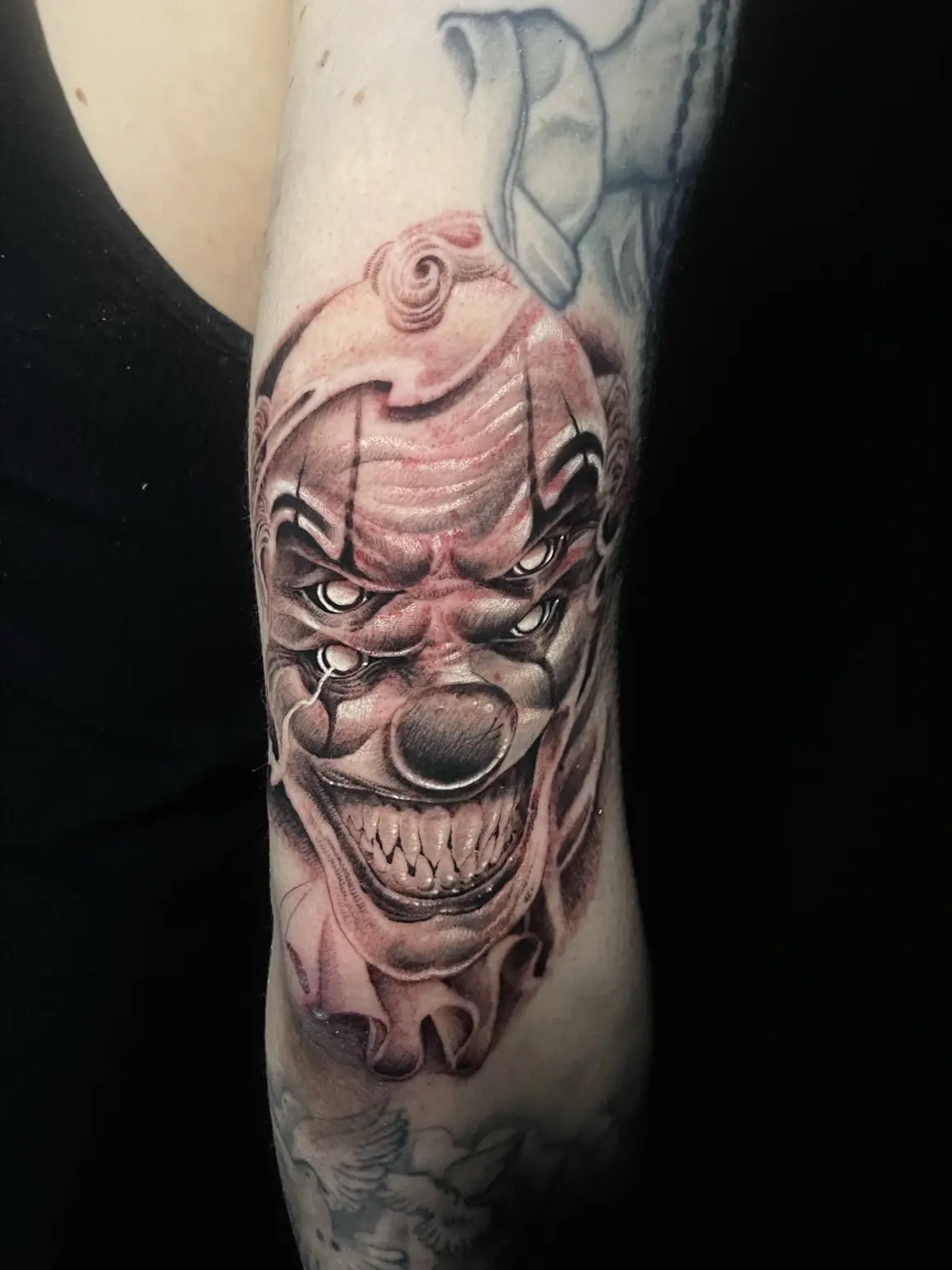 Black-and-gray horror clown upper-arm tattoo by Keith