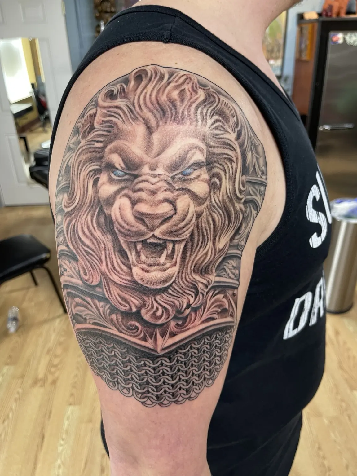 Black-and-gray lion and armor upper-arm tattoo by Keith