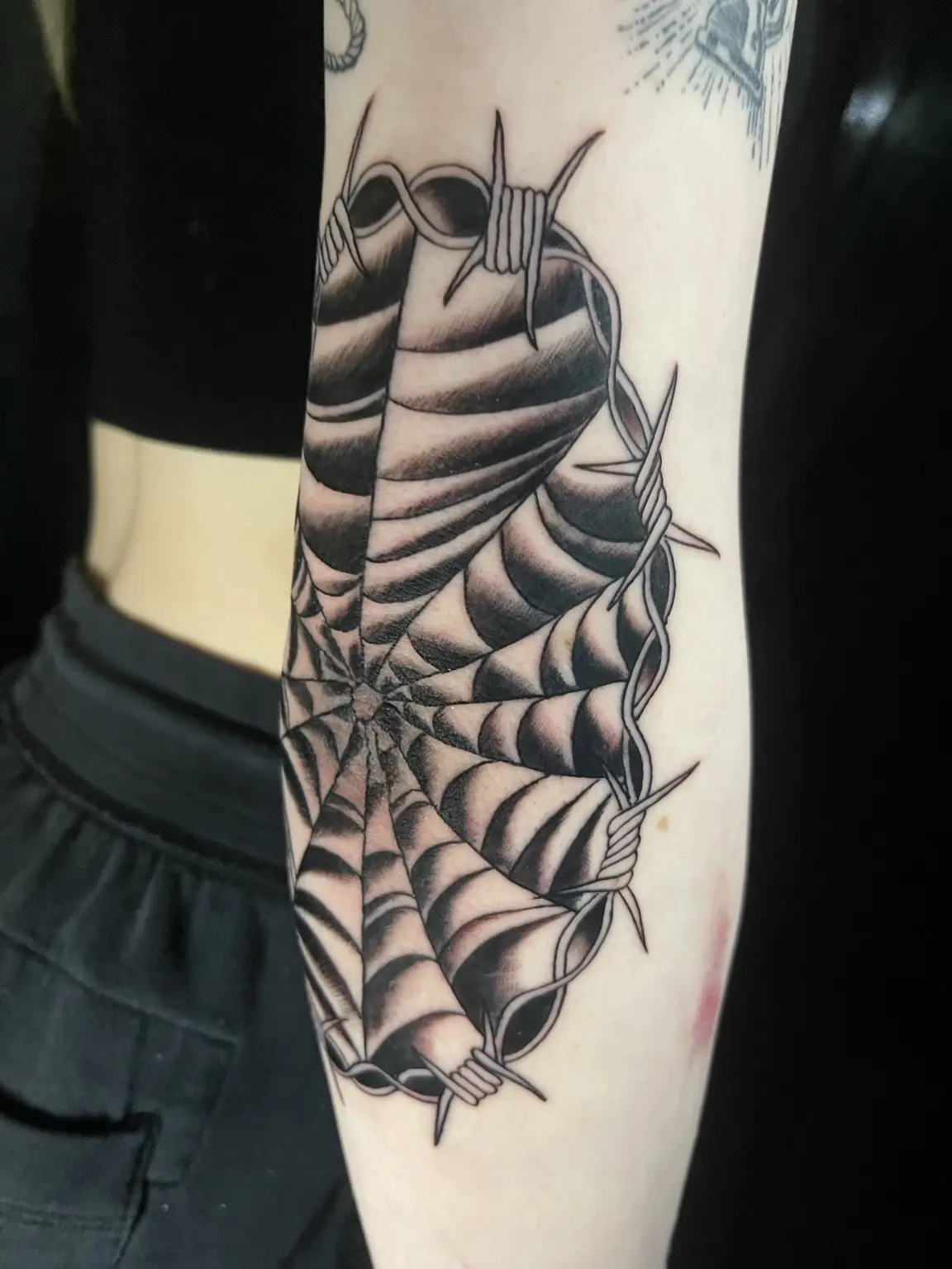 Graphic black-and-gray spiderweb forearm tattoo by Keith