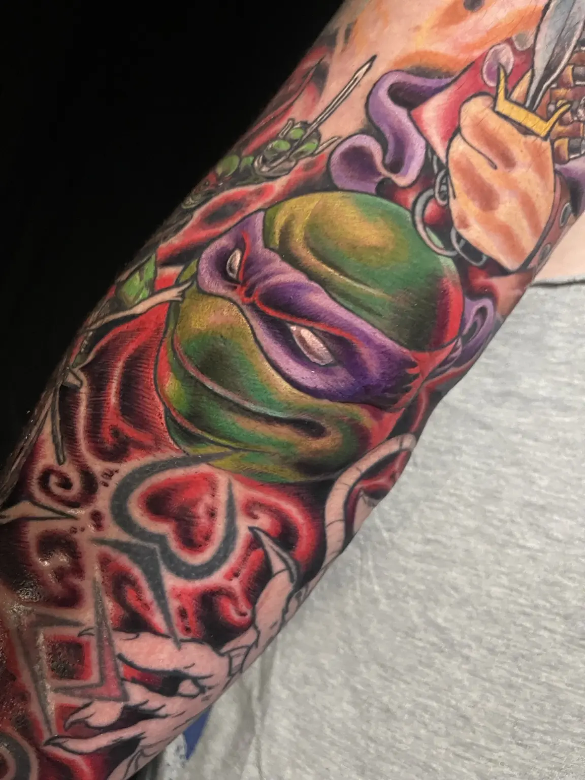 Full-color theatrical mask forearm tattoo by Keith